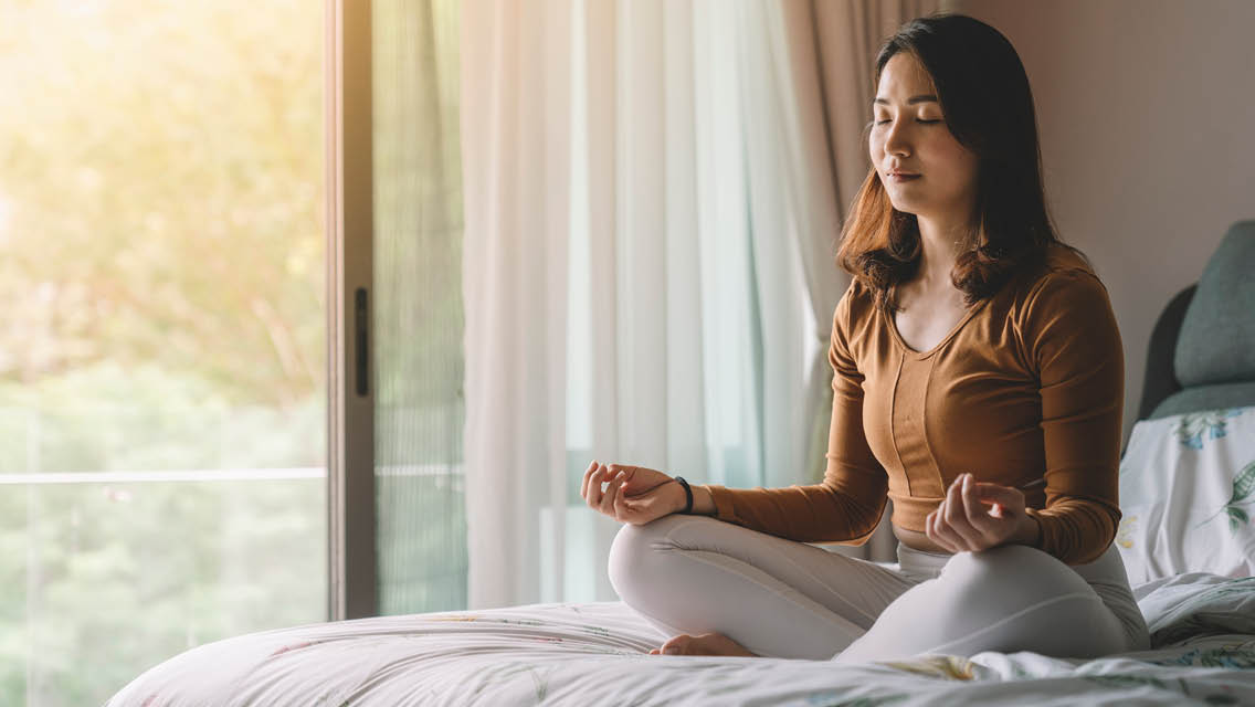 a woman meditates sitting on her bed