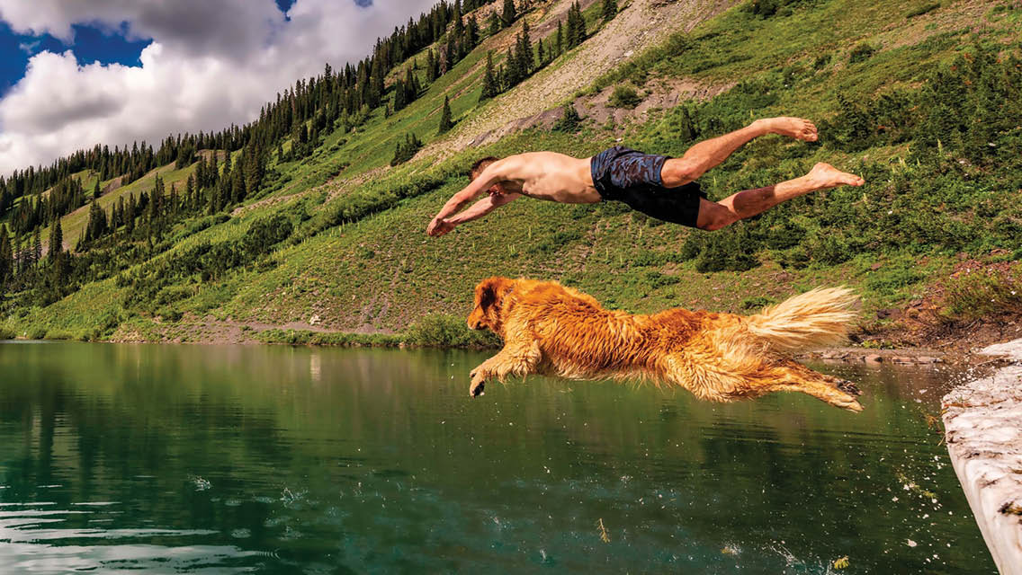 a man and golden retriever dive into a mountain lake