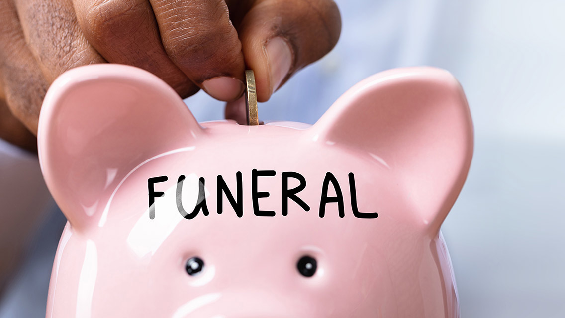 a person puts a coin into a piggy bank with the word funeral on it
