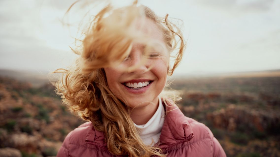 A woman with beautiful red hair blowing in the wind outside.