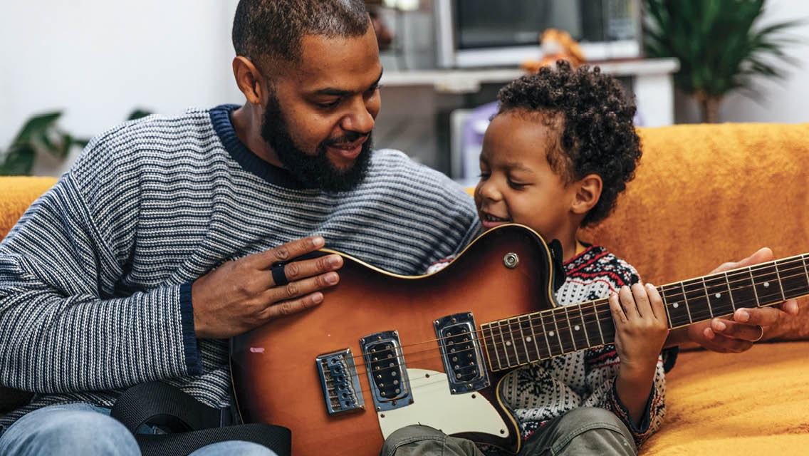 a man teaches his young child guitar