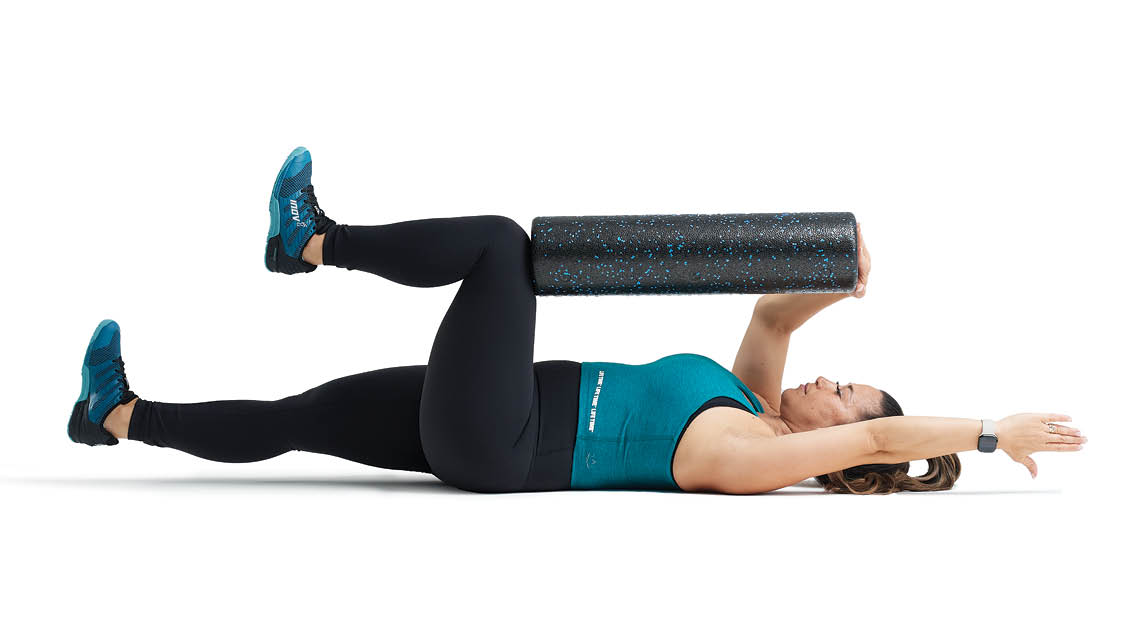 a woman uses a foam roller while performing dead bug