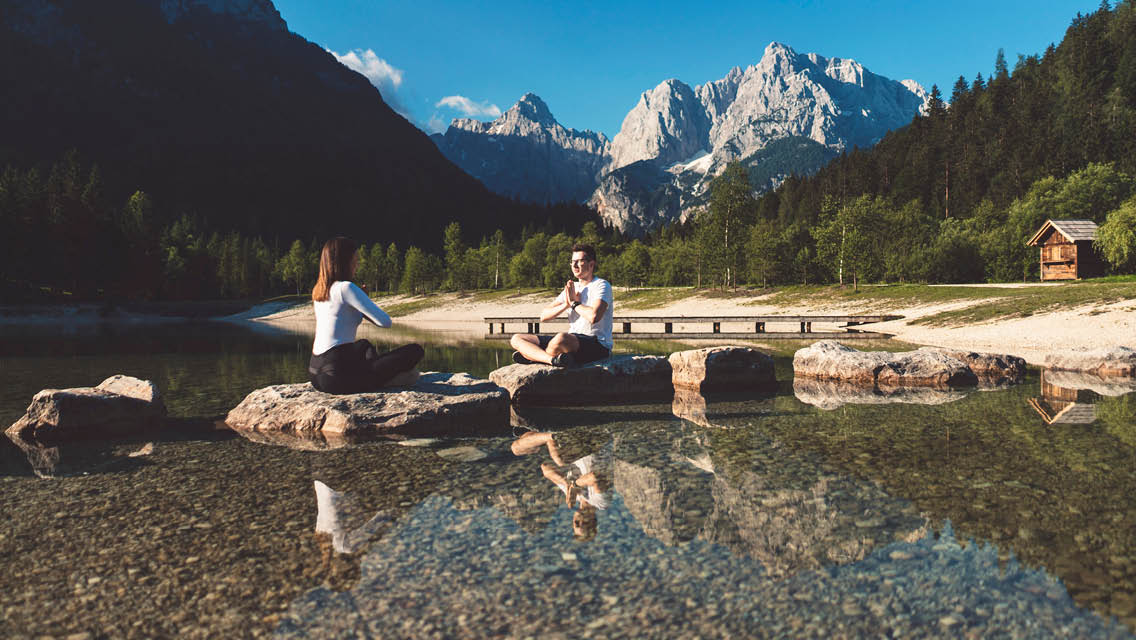 women sit on rocks in a mountain lake meditating
