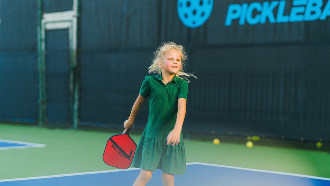A young girl playing pickleball outside at a Life Time court.