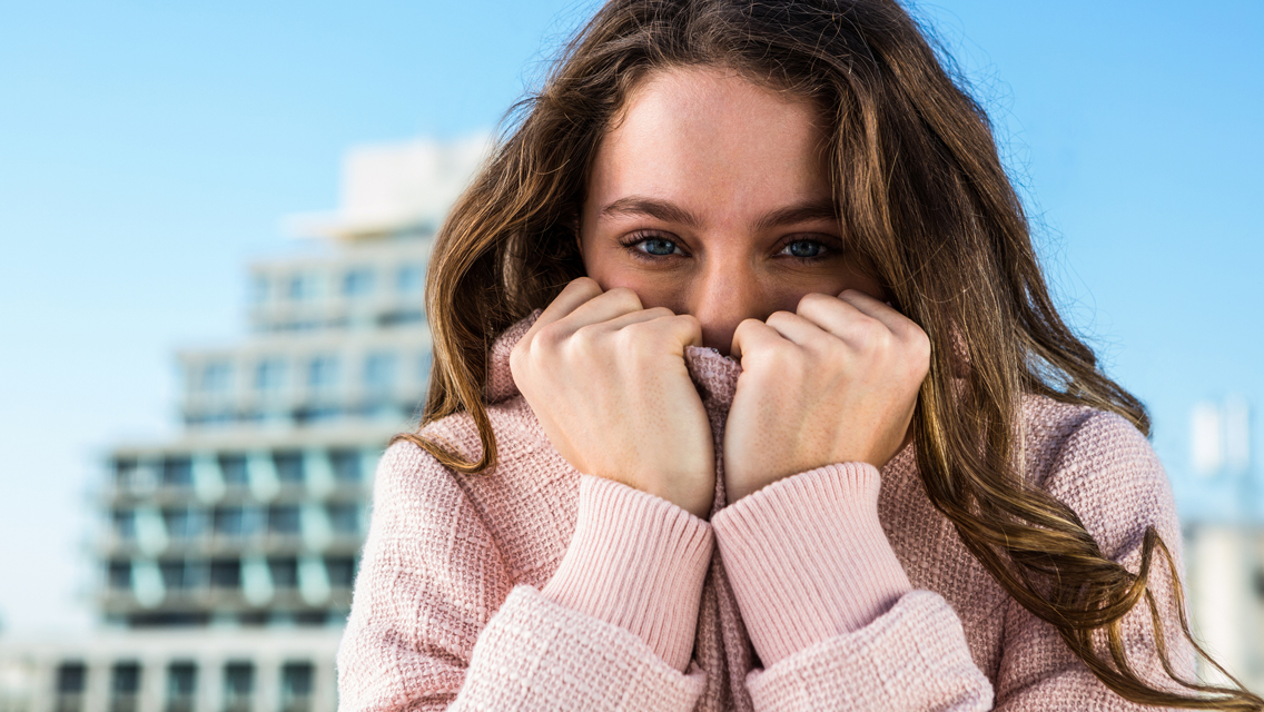 a woman covers her face with the top of her sweater