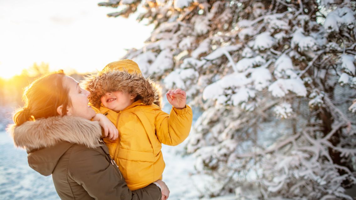 Smiling woman holds a child in a snowy outdoor scene