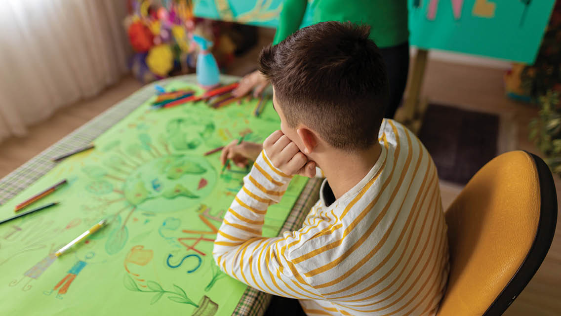a child colors an earth on a large green poster board