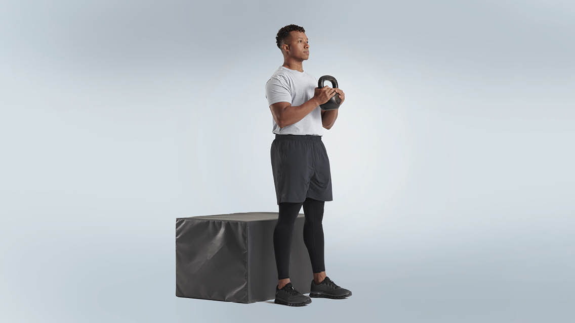 a man holds a kettlebell while standing front of a padded box