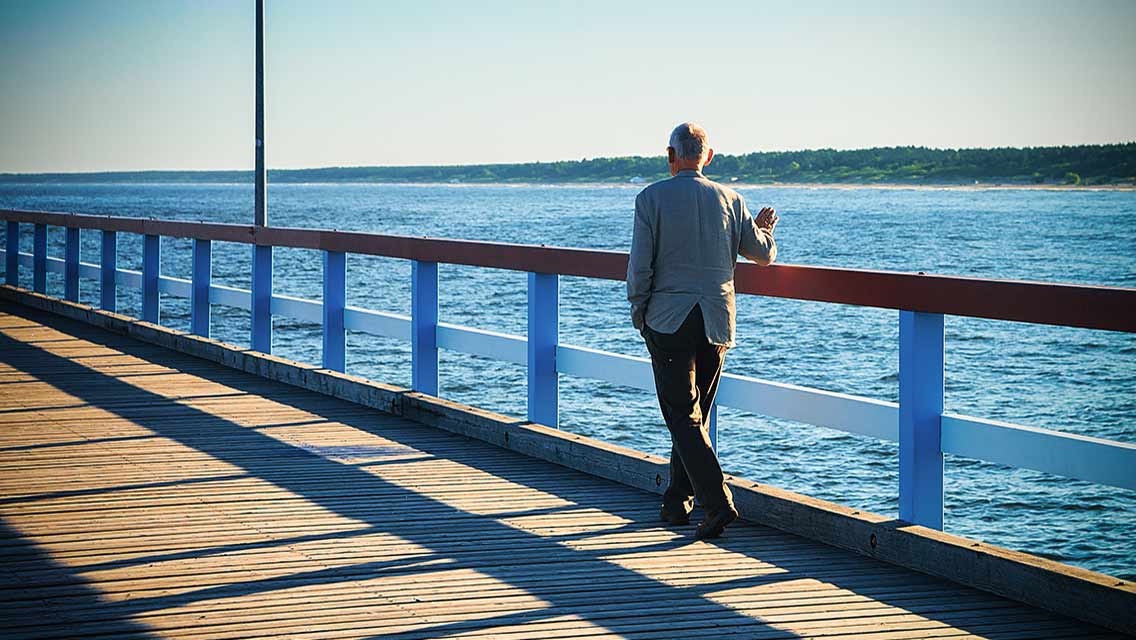 a senior man walks alone on a pier
