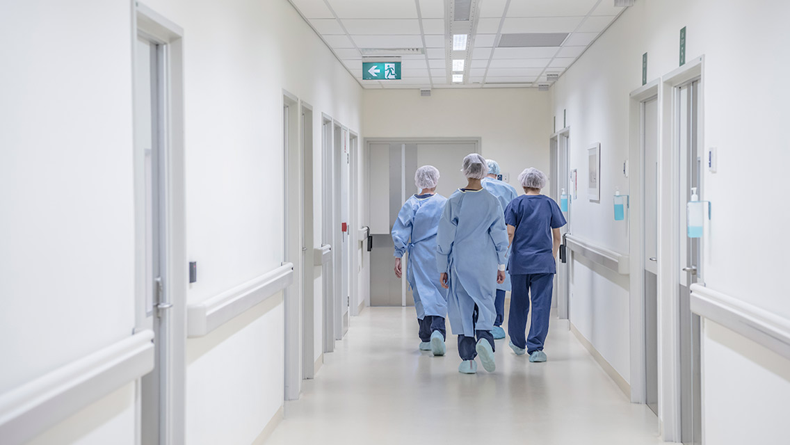 doctors and nurses in scrubs walk down a hospital hallway