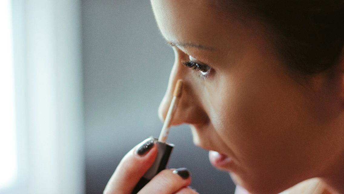 a woman applies concealer to her under eye