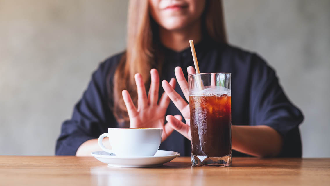 a woman pushes away a cup of coffee and glass of soda