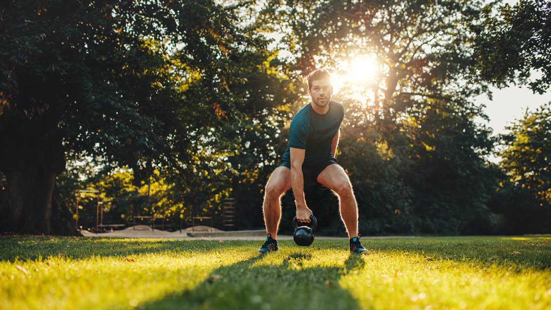 a man uses a kettlebell while working out outside