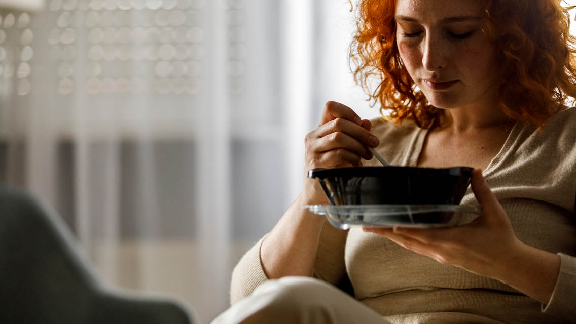 a woman looks sad while eating a microwaveable dinner