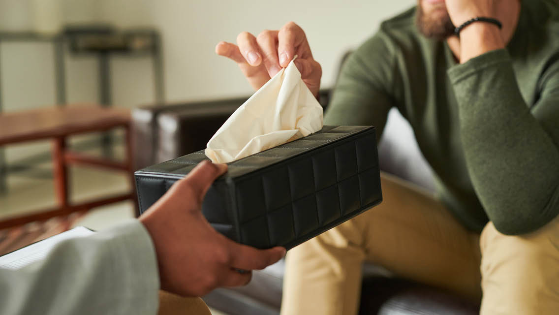 a person hands a tissue box to a sad person