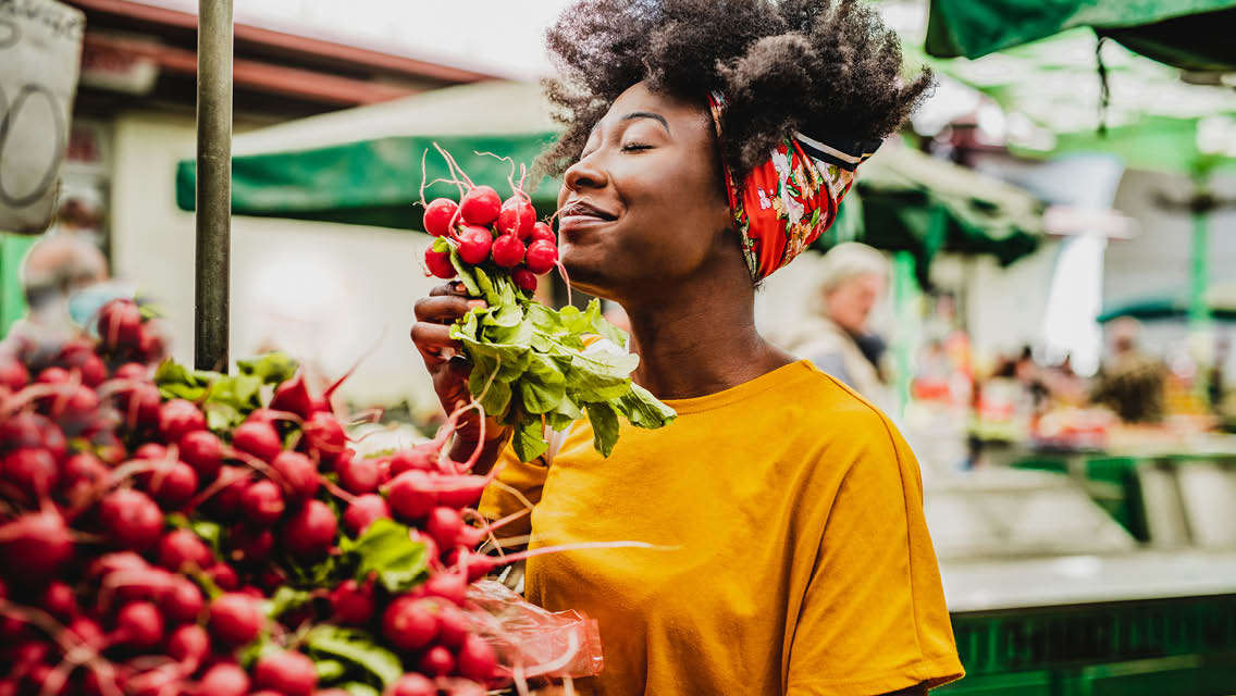 a woman smells radishes at a farmer's market