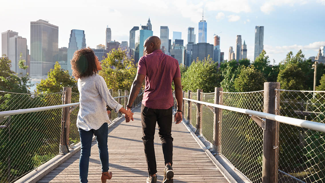 a couple holds hands while walking across a pedestrian bridge