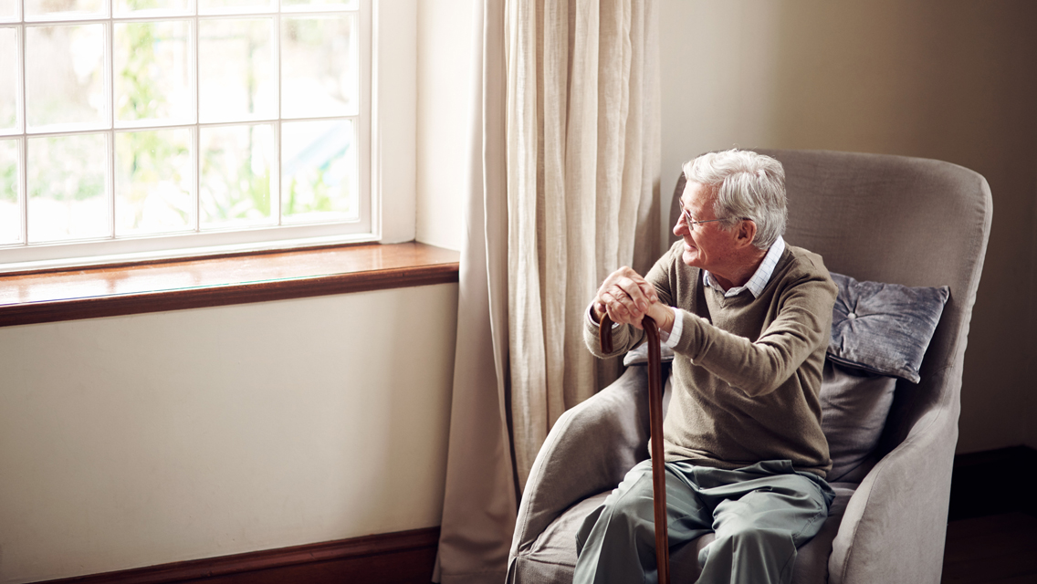 an elderly man sits in a chair looking out the window