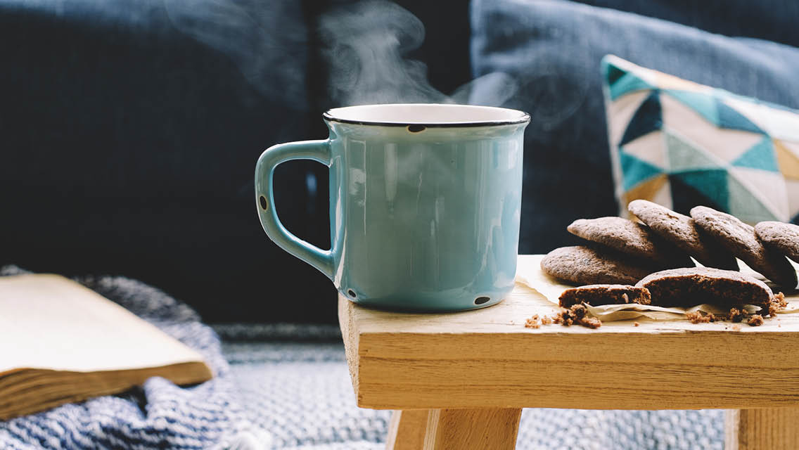 a warm cup of coffee sits next to freshly baked cookies