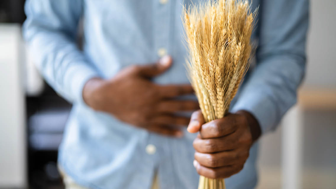 a man holds a shock of wheat with his opposite hand on his stomach