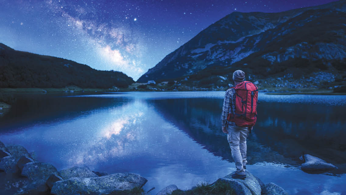 a person stands by a mountain lake at night