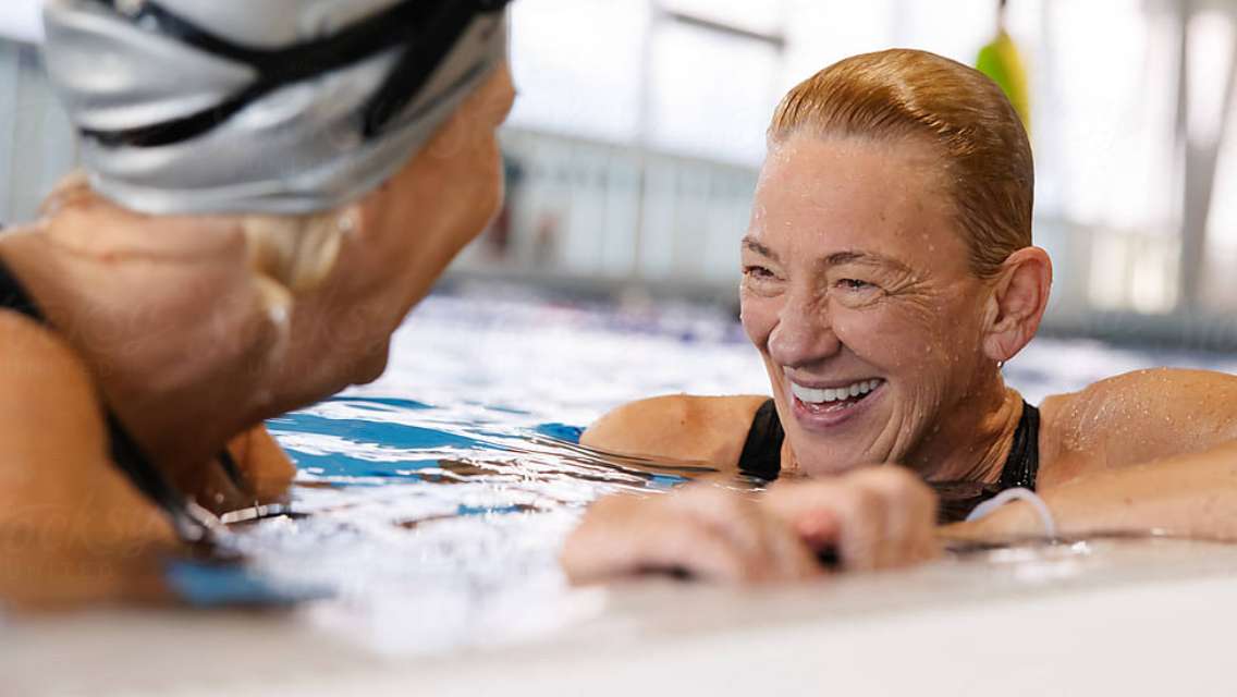 Two adults smiling while in a water fitness class in the pool.