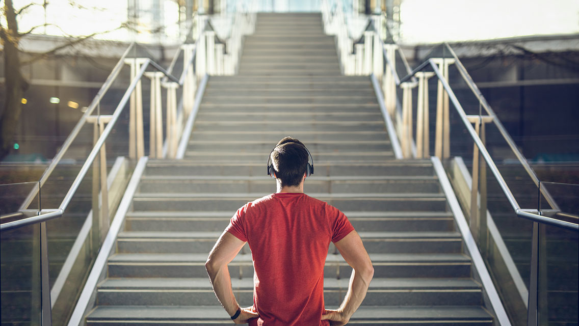 a man in fitness apparel and headphones stands at the base of stairs