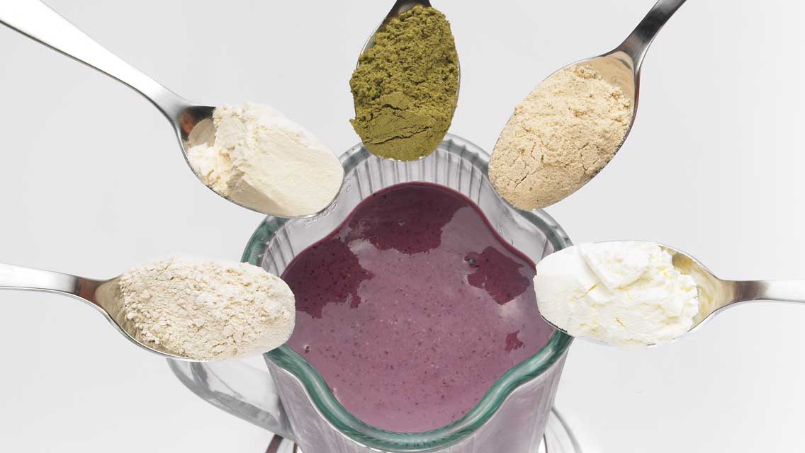 Five different protein powders pointing toward a blender full of smoothie