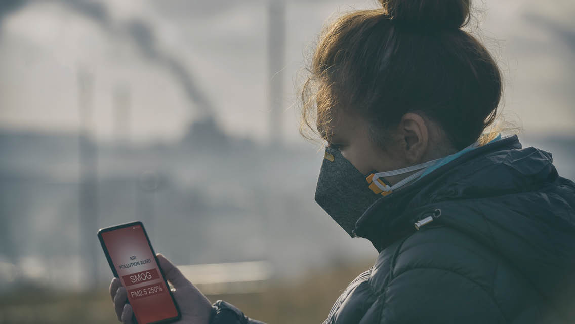 a woman wears a mask while outside looking at her phone with an air quality warning