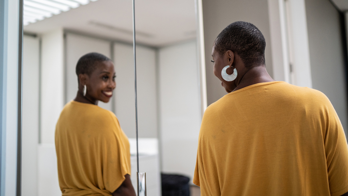a woman looks and smiles confidently at herself in the mirror