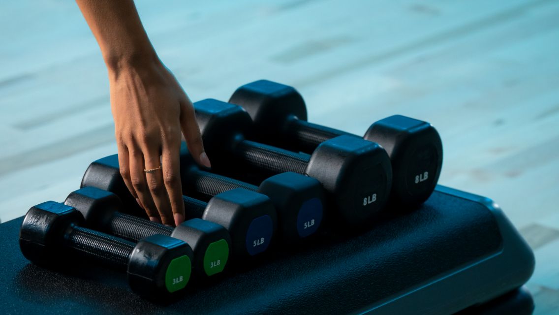 A woman's hand reaching for dumbbells.