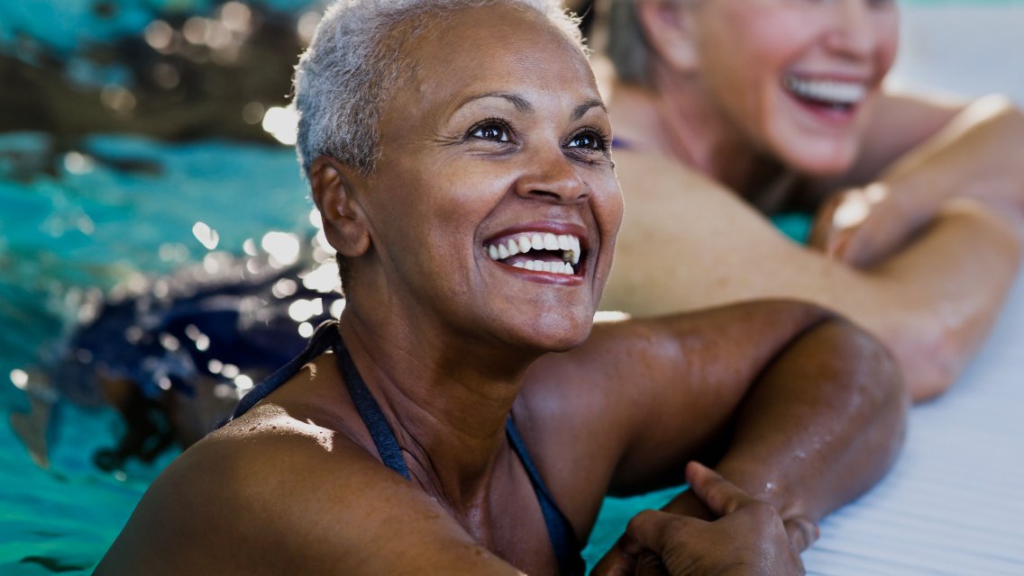 A few women smiling in the pool while taking a break from exercising.