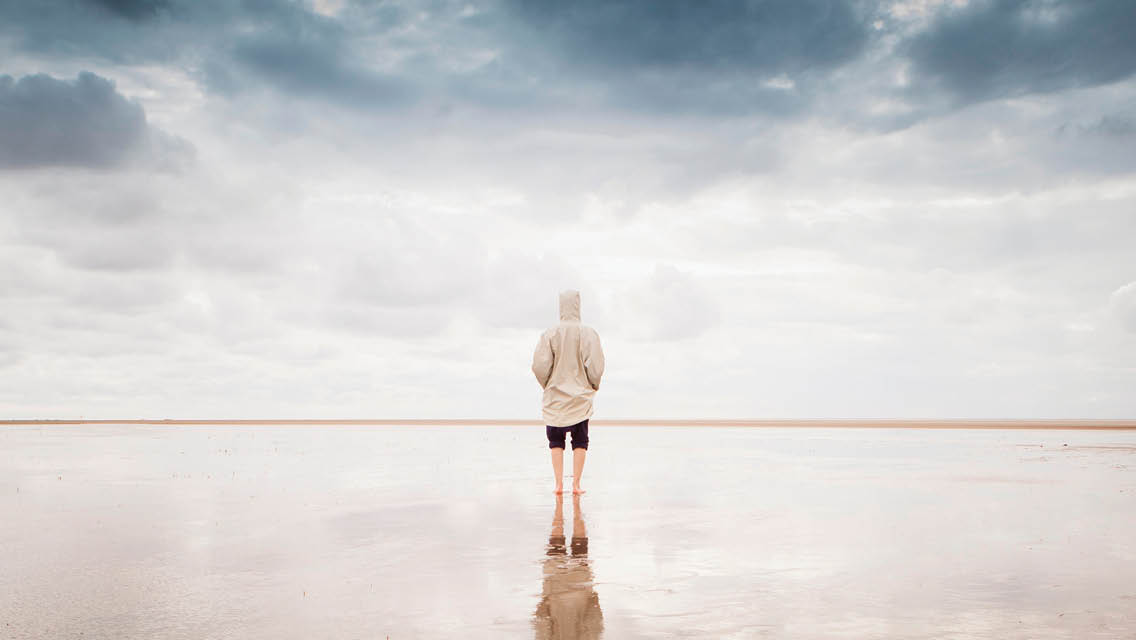 a person stands on a reflective surface with gray clouds all around