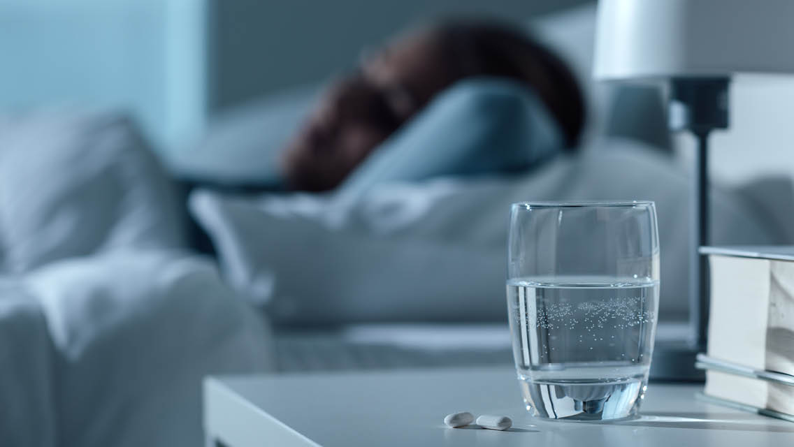 a person sleeping with a glass of water with two supplements by it