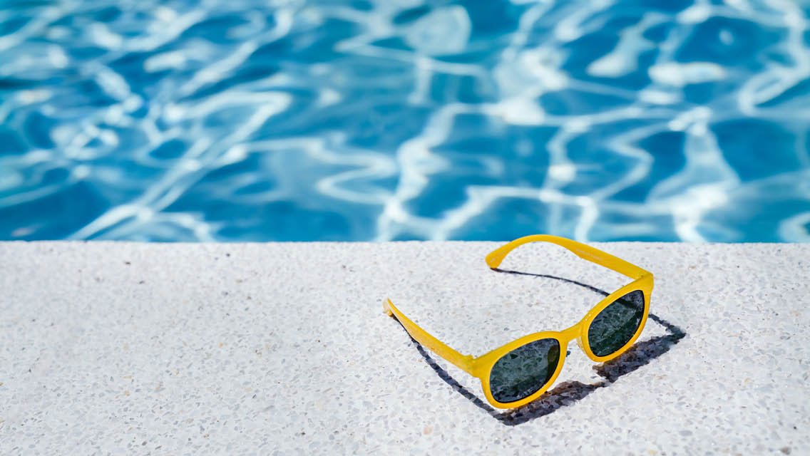 yellow sunglasses sit next to a pool