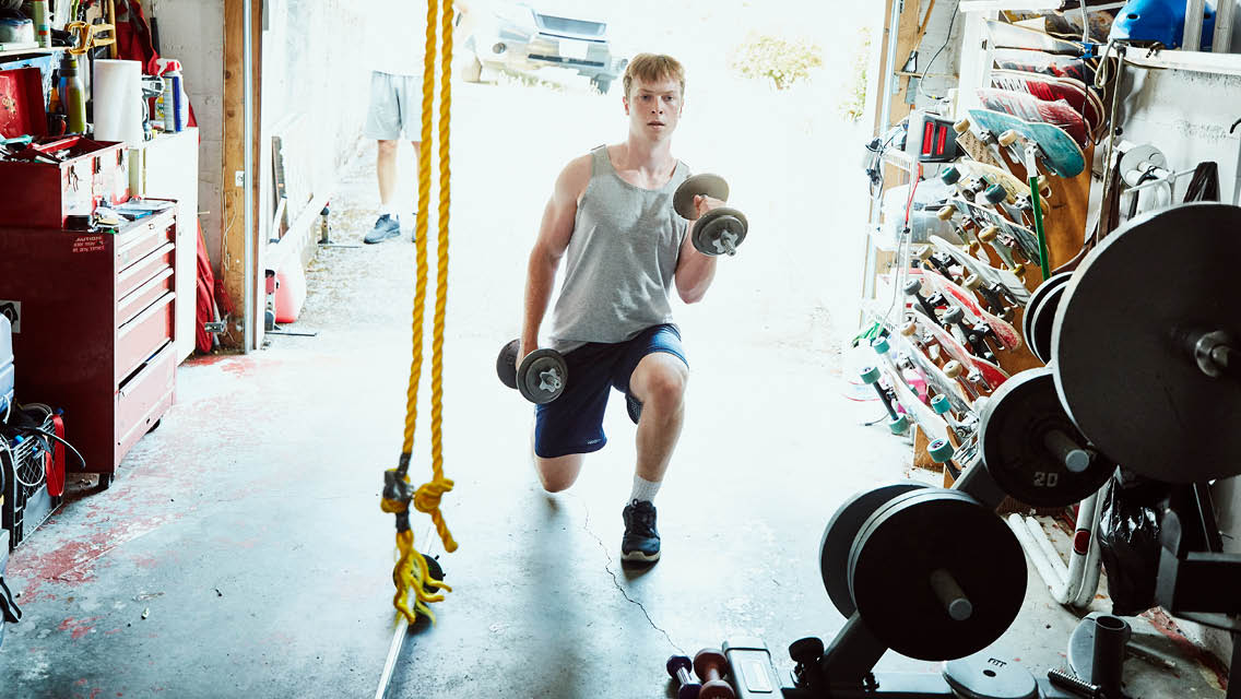 a teen boy lifts weights in his garage