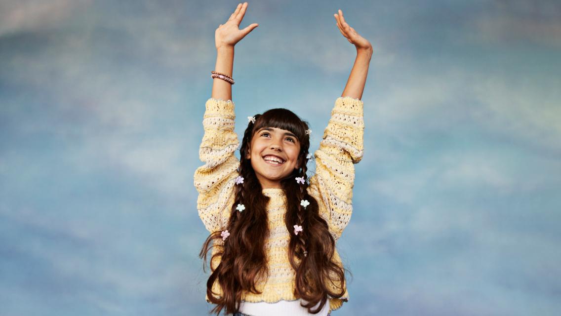 child standing with her arms lifted in the air.