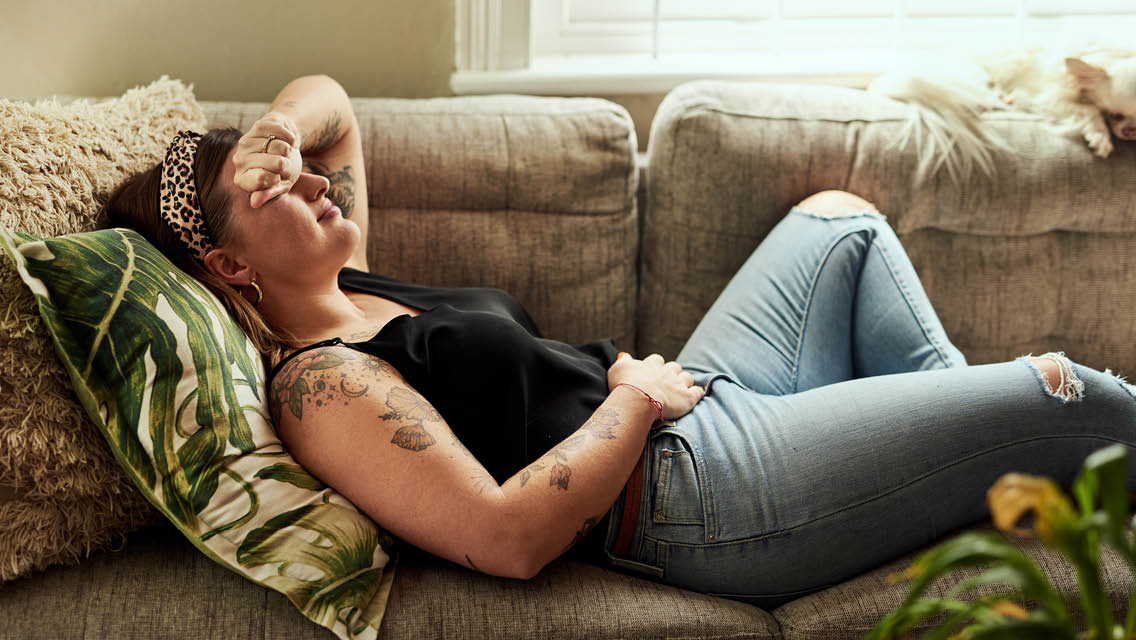 a woman lies on the couch holding her low belly in pain due to endometriosis