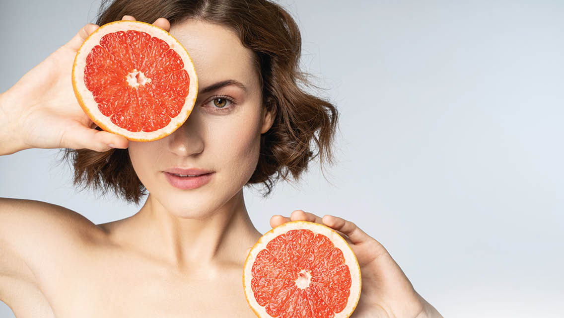 a woman holds sliced grapefruit by her face