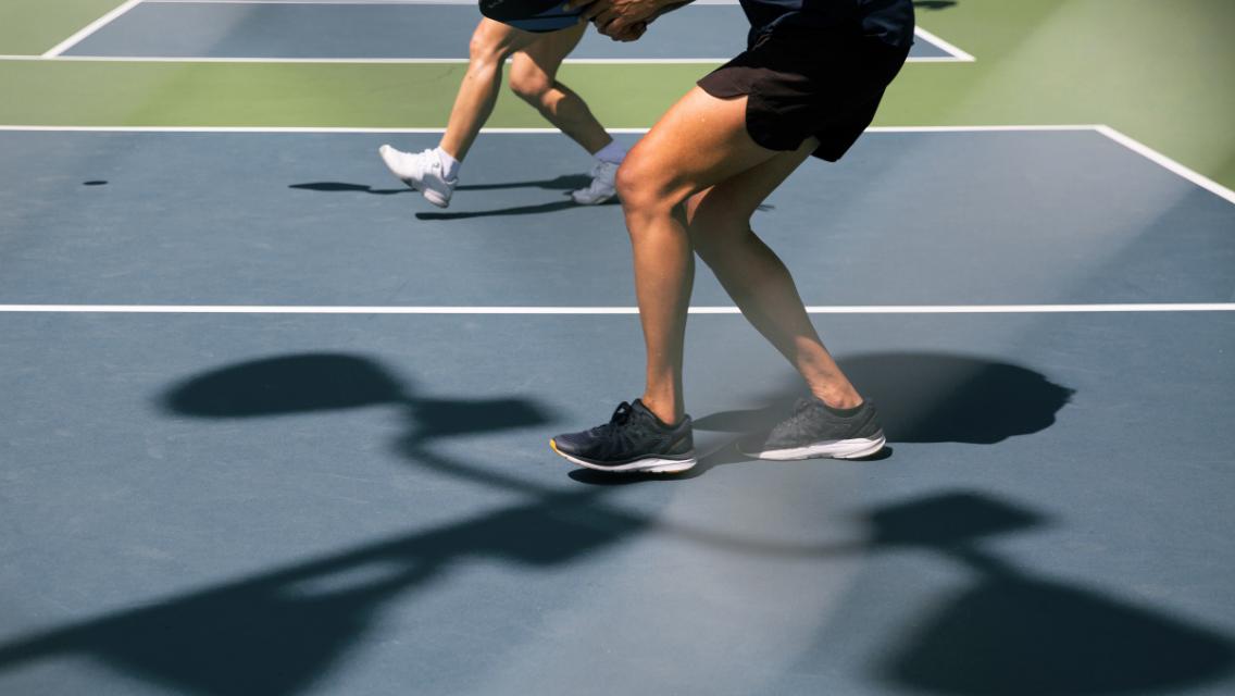 The lower half of two people's bodies who are playing pickleball on an outdoor court.