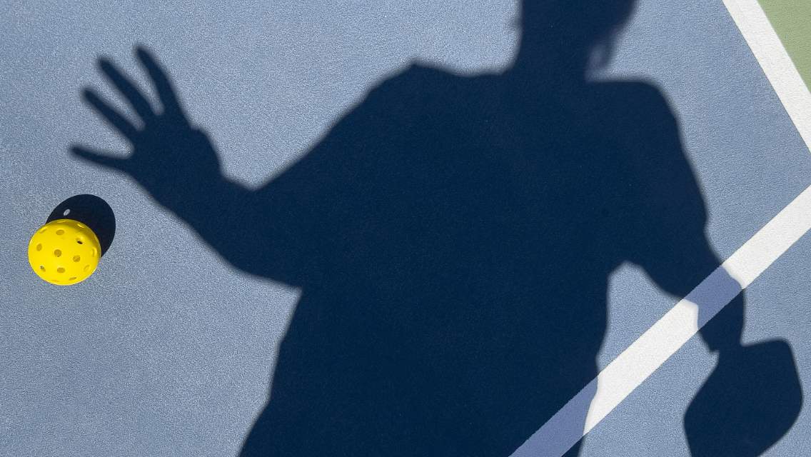 shadow of person on Pickleball court reaching for a ball