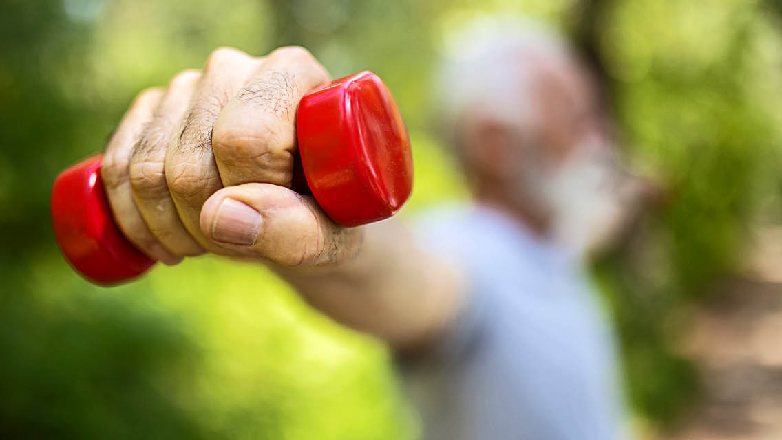 a senior man holding a red weight
