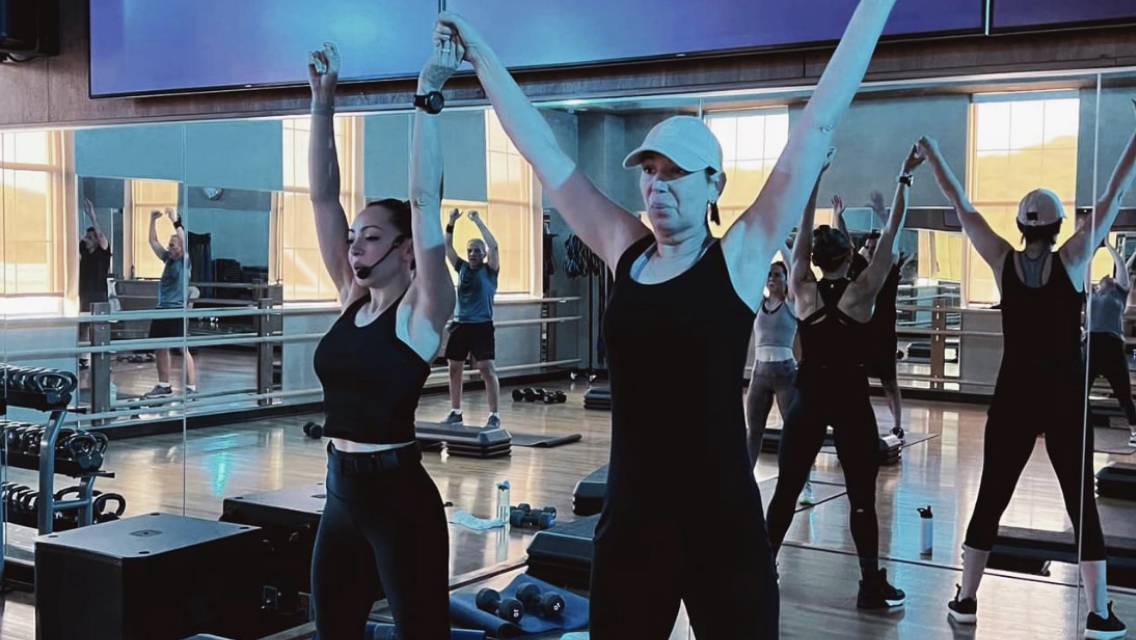 Two people standing with their arms raised above their heads in a Life Time class