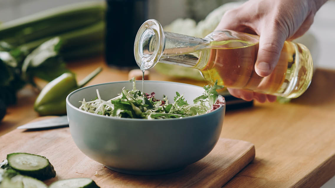 a person drizzles olive oil on a salad