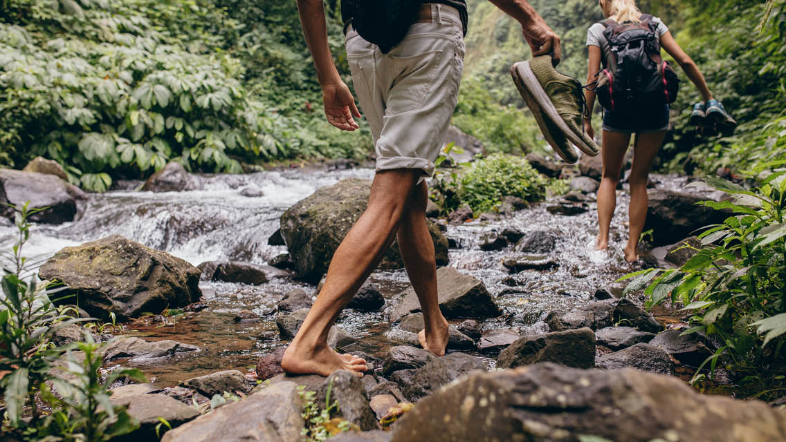 people walk across a river on boulders while barefoot