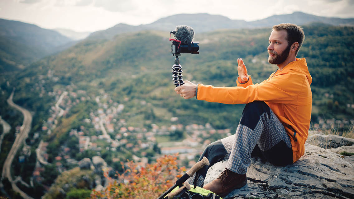 a man sits on the top of a mountain with a video camera filming himself