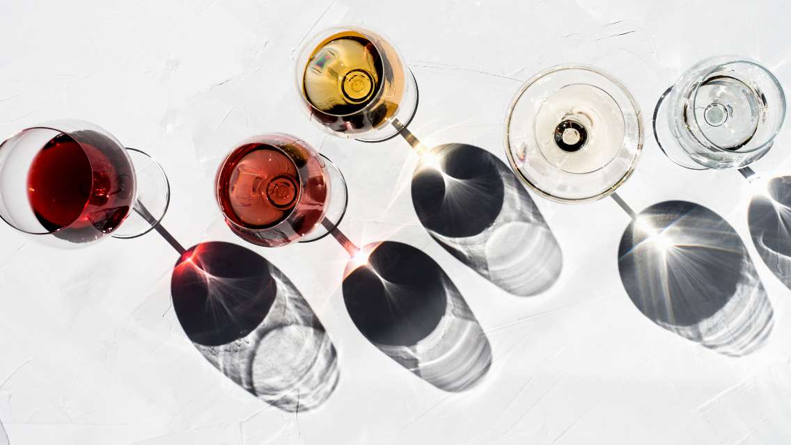 Eight wine glasses full of various beverages