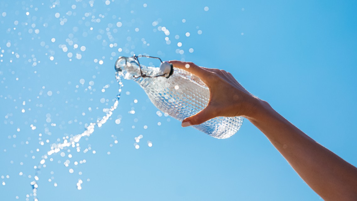 A person holding a glass water bottle, with the water splashing out into the air.