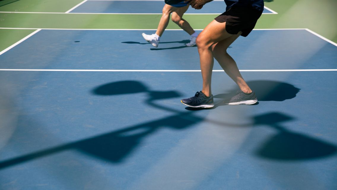 The lower bodies of two individuals playing pickleball on a court.