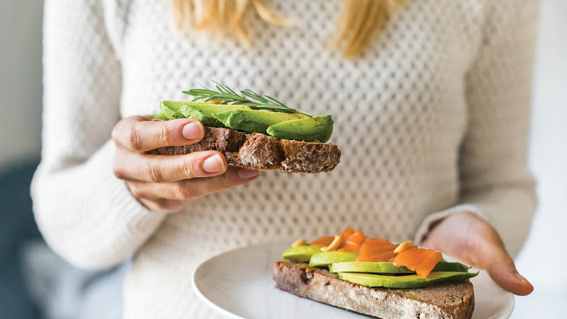 a woman holds a plate with avocado toast